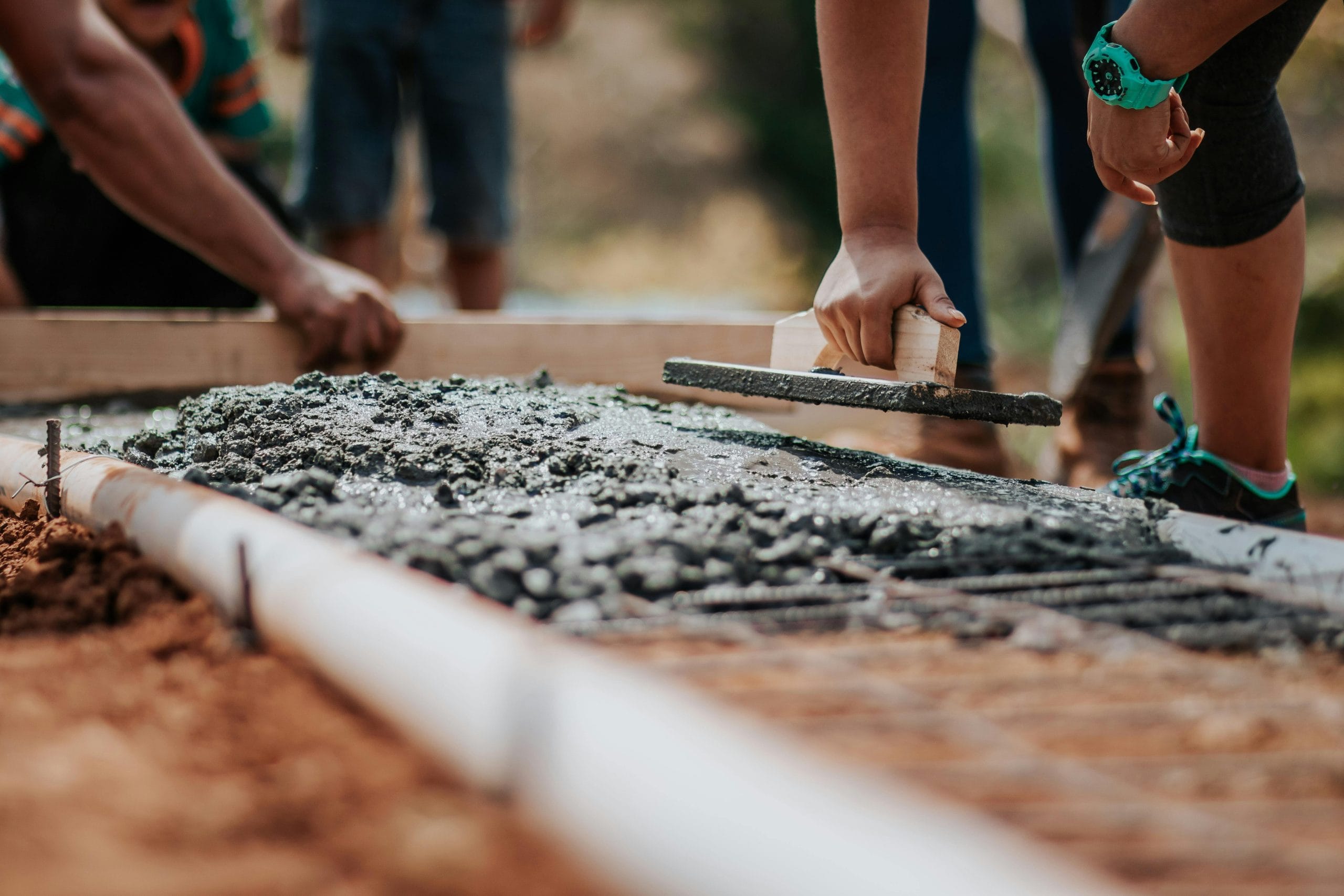 Hands smoothing wet concrete on a construction site, showcasing the building process essential for creating custom homes in Melbourne.