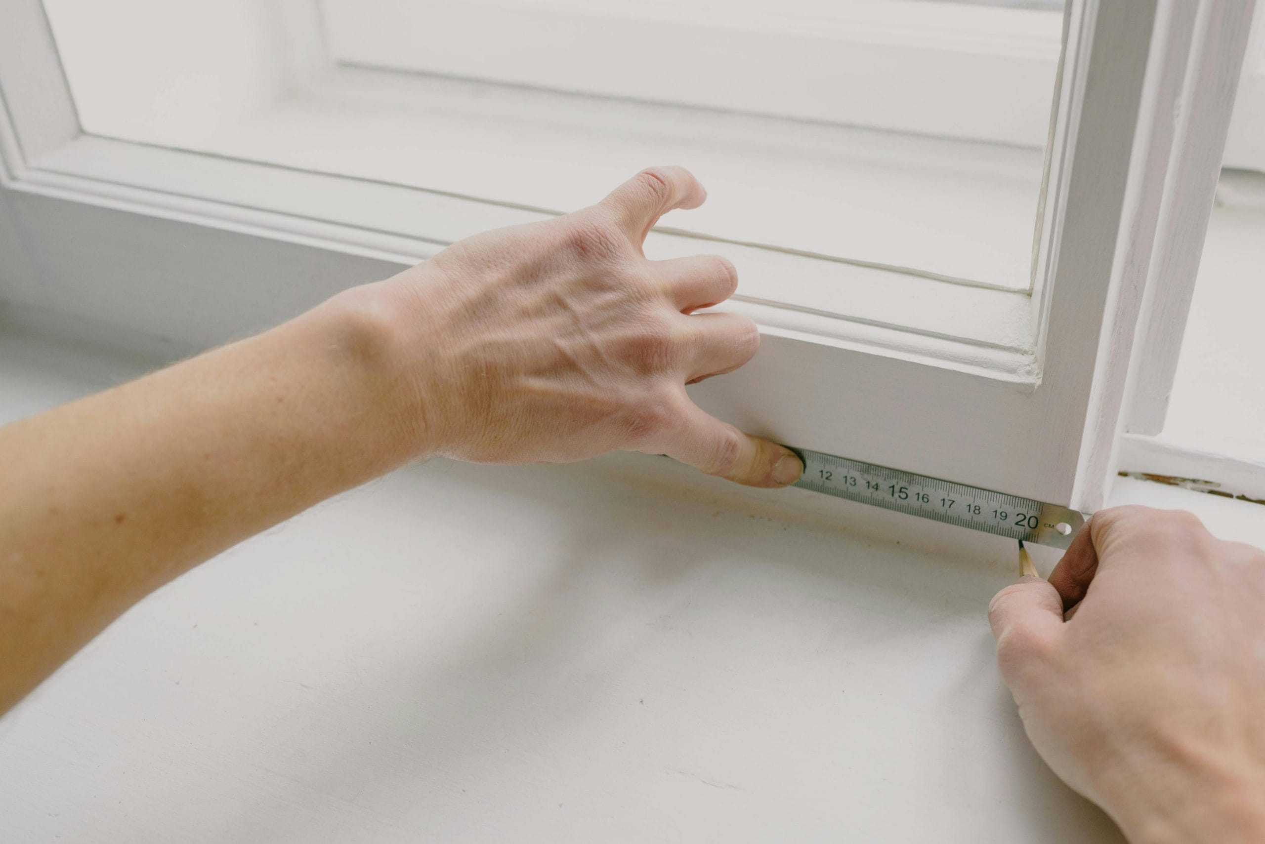 Person measuring a window frame with a ruler, emphasizing precision in architectural drafting and design for custom home building.